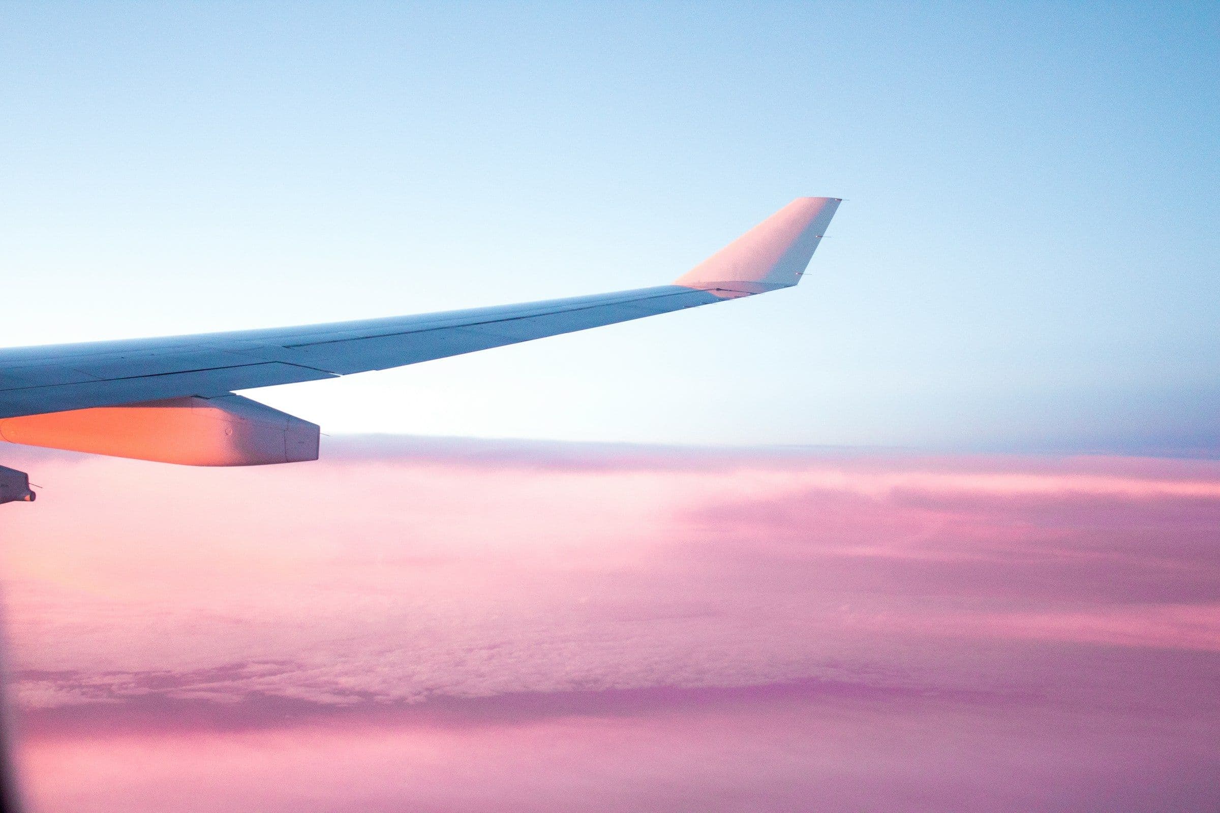 View of an airplane wing in flight with pinkish clouds in the distance